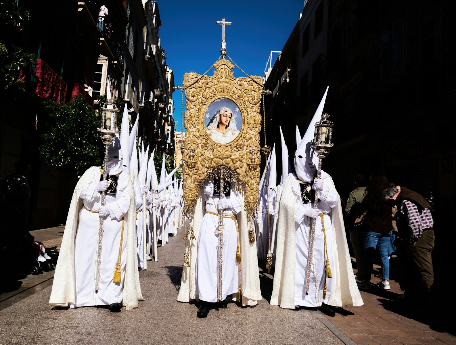 Procesión de Semana Santa con nazarenos de túnica blanca y un paso dorado