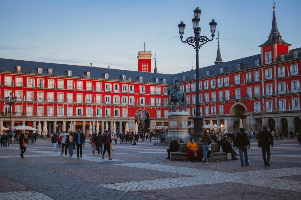 Personas paseando por una calle junto a un edificio rojo en una ciudad española